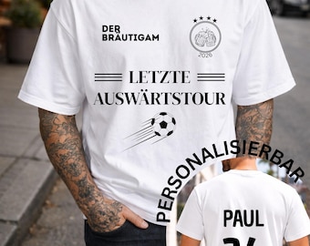 May include: White t-shirt with black text and graphics. The front features the words "DER BRÄUTIGAM" and "LETZTE AUSWÄRTSTOUR" along with a soccer ball graphic. The back of the shirt has the name "PAUL" and the number "26".