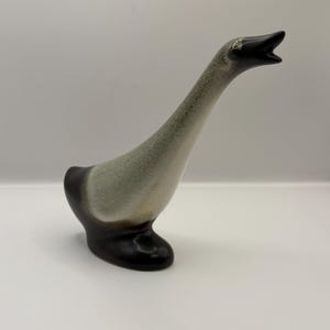 May include: A ceramic goose figurine with a long neck and open beak. The goose has a black base and head, with a gray and white body. The figurine is a decorative item.
