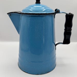 May include: A vintage blue enamelware coffee pot with a black handle and lid knob. The pot has a speckled finish and a spout for pouring. The handle is made of wood. The pot is designed for stovetop use.