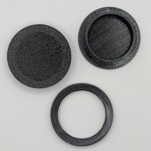May include: Three black circular components with a textured finish. Two pieces are solid discs with a raised rim and a recessed center, while the third piece is a thin, open ring with a matching black finish and visible layered texture.