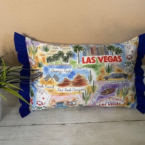 May include: A blue and white pillow with a colorful illustration of Las Vegas landmarks and the text "LAS VEGAS".