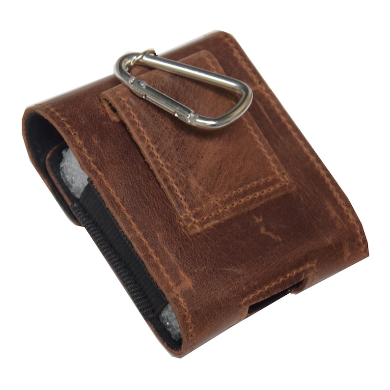 May include: A brown leather phone case with a silver carabiner clip. The case has a textured surface and a black elastic side. The case is designed to be worn on a belt or bag.