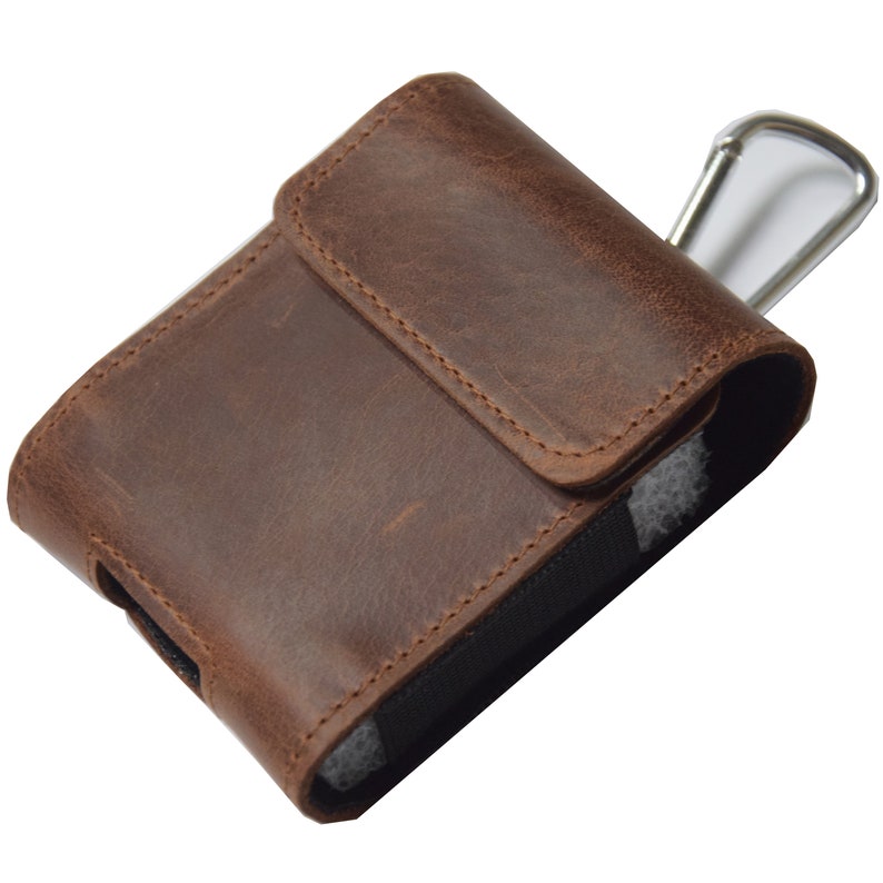 May include: A brown leather cigarette case with a flap closure. The case has a rectangular shape and a silver-colored metal clip is visible. The leather has a textured appearance.