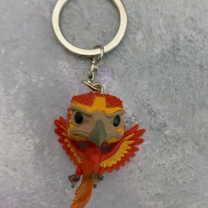 May include: A red and yellow phoenix keychain with a silver key ring. The phoenix is in a flying pose with its wings spread out.