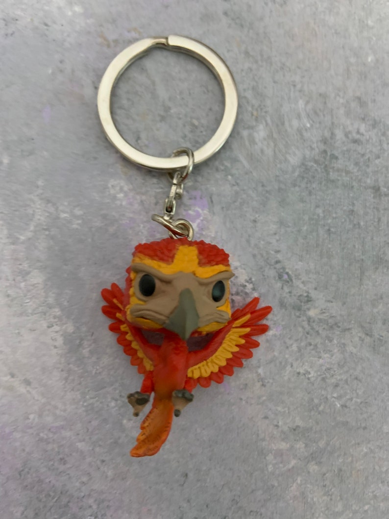 May include: A red and yellow phoenix keychain with a silver key ring. The phoenix is in a flying pose with its wings spread out.