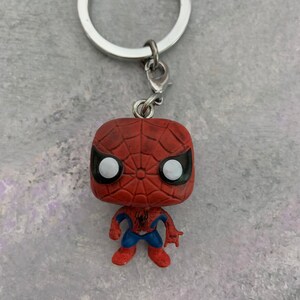 May include: A red and blue Spider-Man keychain with a silver key ring. The keychain is a small, stylized figure of Spider-Man with a web design on his chest.