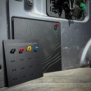 May include: Black magnetic cover with a topographic map design and colorful hooks. A smaller black panel displays additional hooks. The text "PRO POWER ONBOARD MAGNETIC COVER" is visible. The hooks are black, red, yellow, and blue.