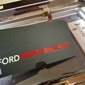 May include: A black and gray topographical map design with the text "FORD PERFORMANCE" in red and white lettering.