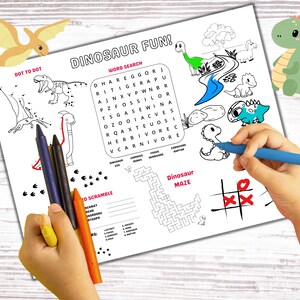 Puede incluir: Una hoja de actividades imprimible en blanco y negro con tem&aacute;tica de dinosaurios. La hoja incluye una actividad de unir puntos, una b&uacute;squeda de palabras, una palabra revuelta, un laberinto y un juego de tres en raya. La mano de un ni&ntilde;o sostiene l&aacute;pices de colores y colorea la hoja.