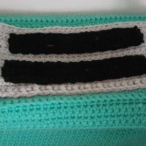 May include: A teal crocheted bag with a gray and black crocheted panel on the front. The panel has two black stripes.