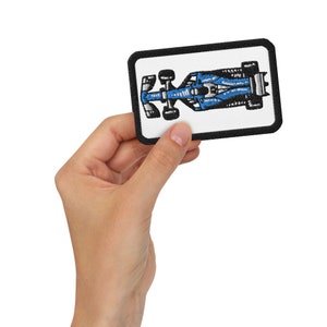 Op de afbeelding: Een geborduurde patch met een raceauto die van bovenaf wordt bekeken, in blauw en zwart.