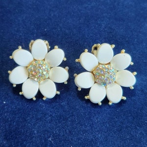 May include: A pair of white flower-shaped clip-on earrings with gold accents and iridescent rhinestones in the center.