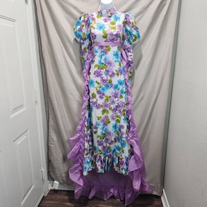 May include: A long white dress with a purple floral print and a lavender ruffle trim. The dress has a high neck and puffed sleeves.