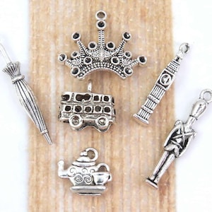 May include: A set of six silver charm pendants featuring London themed designs. The charms include a crown, a double-decker bus, a teapot, a London telephone booth, a soldier, and an umbrella.