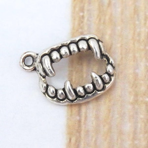 May include: Silver charm in the shape of a set of fangs. The charm has a loop at the top for attaching to a necklace or bracelet.