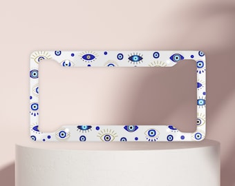 May include: White license plate frame with a pattern of blue and gold evil eyes.
