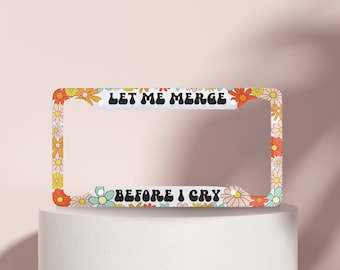 May include: White license plate frame with a floral design and the text "Let me merge before I cry".