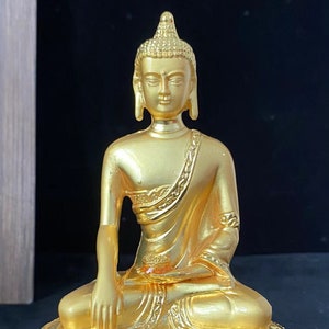 May include: A gold-colored Buddha statue sitting in a meditative pose on a lotus base. The statue is detailed with intricate carvings and a serene expression.