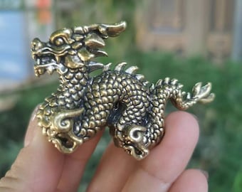 Puede incluir: Una pequeña figura de dragón de color dorado con detalles intrincados. El dragón está enroscado con su cola envuelta alrededor de su cuerpo.