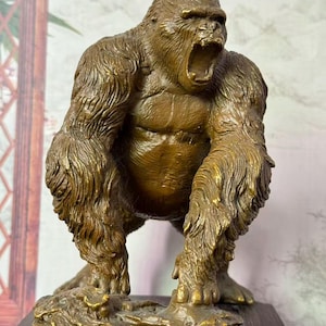 Puede incluir: Escultura de gorila de bronce en pose rugiente, con textura de pelaje detallada y boca abierta. El simio está de pie sobre una base texturizada, mostrando la intrincada artesanía de la estatua. Es un artículo decorativo.