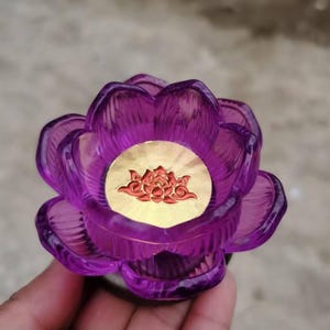 May include: A purple, flower-shaped decorative object with a gold-coloured centre. The centre features a red floral design. The object is made of a translucent material, and the petals are intricately detailed.