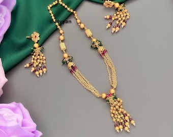 May include: A gold necklace and earrings set with a beaded tassel design. The necklace features a chain with small gold balls and green and red beads. The earrings have a flower design with a red center and a beaded tassel.