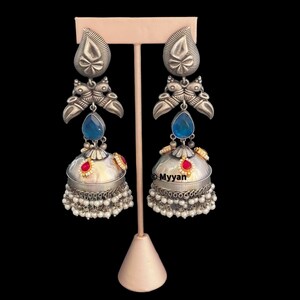 May include: A pair of silver earrings with blue and red stones, pearl accents, and a bell-shaped design. The earrings are displayed on a stand.
