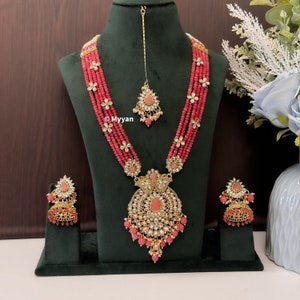 May include: A pink and gold beaded necklace set with a large pendant and matching earrings. The necklace has multiple strands of beads and the pendant is decorated with intricate details.