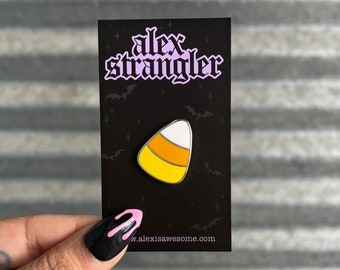 May include: A yellow, orange, and white candy corn enamel pin on a black card with the text "alex strangler" and the website "w.alexisawesome.com".