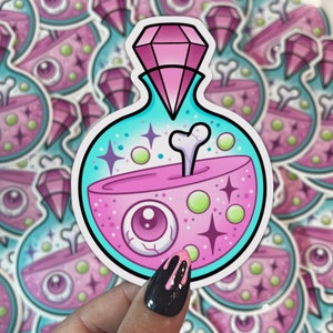 May include: A pink and blue potion bottle sticker with a pink diamond on top, a bone sticking out of the potion, and a pink eye inside. The sticker is on a white background.