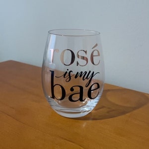 May include: A clear glass wine glass with the text "rosé is my bae" printed in black on the side.