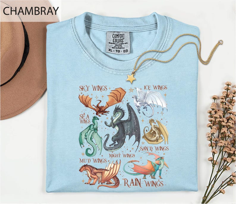 A light blue t-shirt with a graphic design of various dragon-like creatures, including sea, night, mud, sand, rain, and ice wings, along with the text "Sky Wings", "Ice Wings", "Sea Wings", "Night Wings", "Mud Wings", and "Sand Wings".