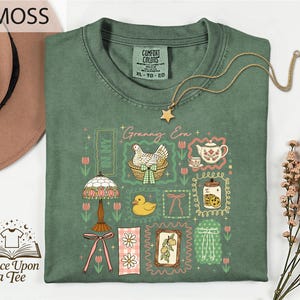 a green t-shirt with a variety of colorful illustrations and text, including a lamp, flowers, a teapot, and a bird, along with the text "MOSS" and "Once Upon a Tee".