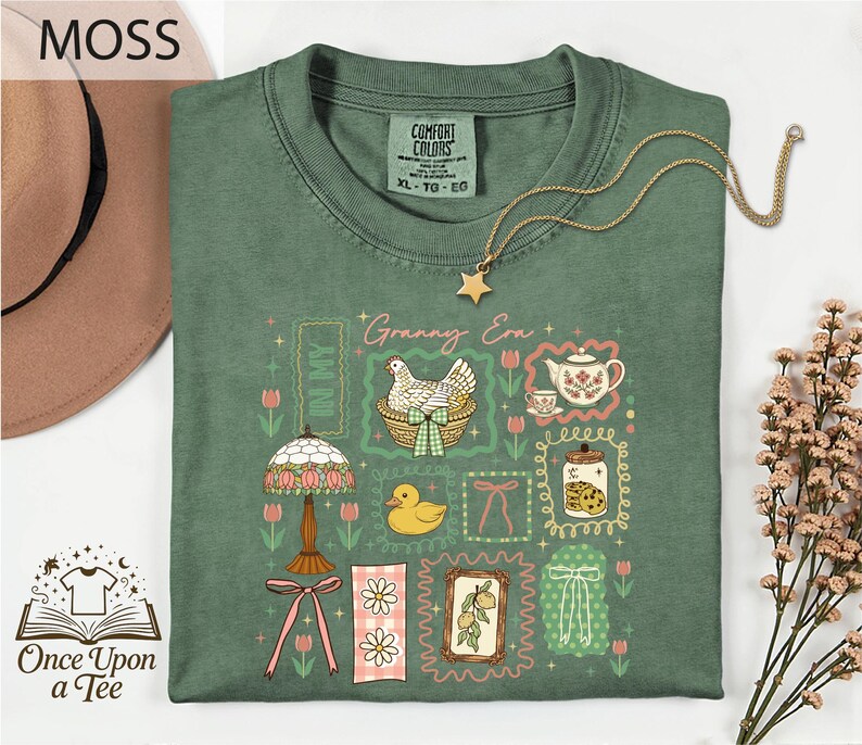 a green t-shirt with a variety of colorful illustrations and text, including a lamp, flowers, a teapot, and a bird, along with the text "MOSS" and "Once Upon a Tee".