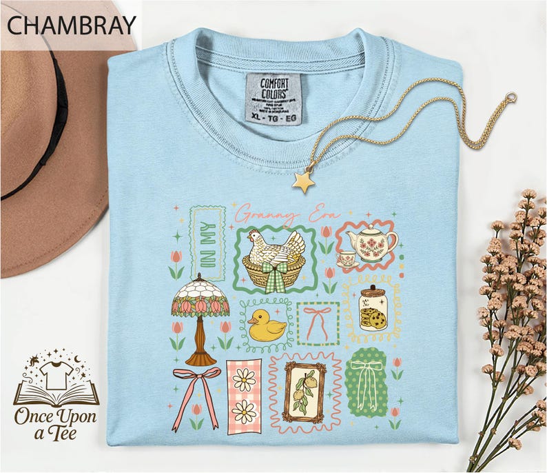 a light blue t-shirt with a colorful graphic design, including a lamp, teapot, flowers, and a bird, along with a gold chain and a star pendant.