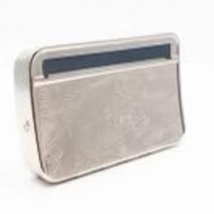 May include: A small, rectangular, silver-coloured metal box with a beige fabric exterior. The fabric has a subtle, embossed pattern. The box has a zipper closure.