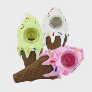 Puede incluir: Tres pipas novedosas con forma de cono de helado. Una es verde claro, otra blanca y otra rosa. Cada una tiene una base de cono marrón, chispas de colores y un cuenco transparente. Las pipas están diseñadas para parecerse a conos de helado.