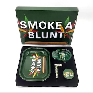 May include: A green box set with the words "SMOKE A BLUNT" and cannabis leaf designs. The set includes a tray, ashtray, grinder, and a round container, all with matching designs. A blunt is visible in the tray.