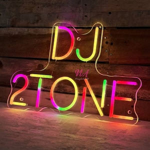 May include: A neon sign with the text "DJ 2TONE" in a colorful, multi-colored design. The sign is made of clear acrylic and has a wavy, irregular shape.