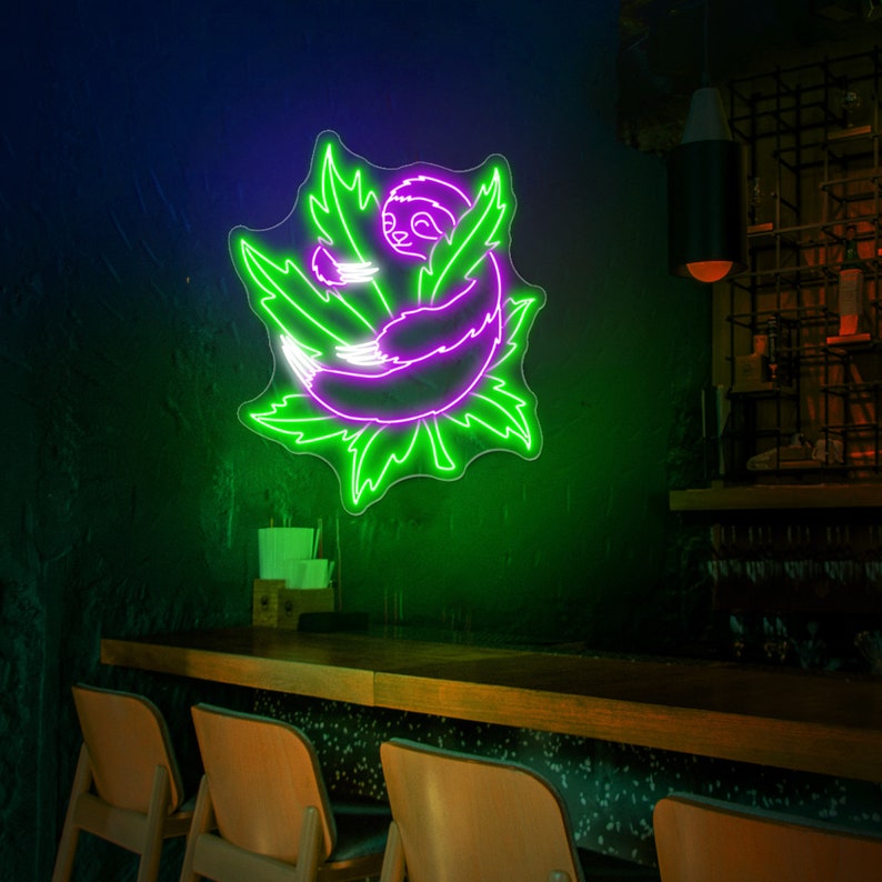 Pode incluir: Um letreiro de n&eacute;on que representa um bicho-pregui&ccedil;a roxo enroscado dentro de uma folha verde. O letreiro est&aacute; montado em uma parede verde escura acima de um balc&atilde;o de bar de madeira.