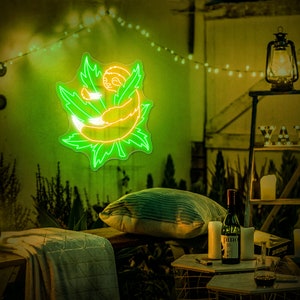 Pode incluir: Um letreiro de n&eacute;on verde que representa um bicho-pregui&ccedil;a enroscado em uma folha. O letreiro est&aacute; pendurado em uma parede em um c&ocirc;modo com pouca luz com luzes de corda e uma mesa de madeira com uma garrafa de vinho e um copo.