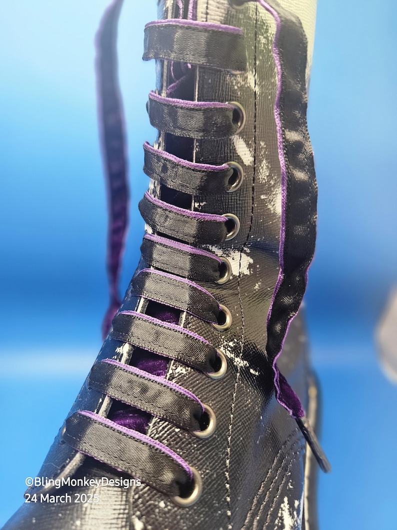 May include: Close-up of a black and white boot with purple laces. The boot has a white paint splatter design and a black ribbon trim.