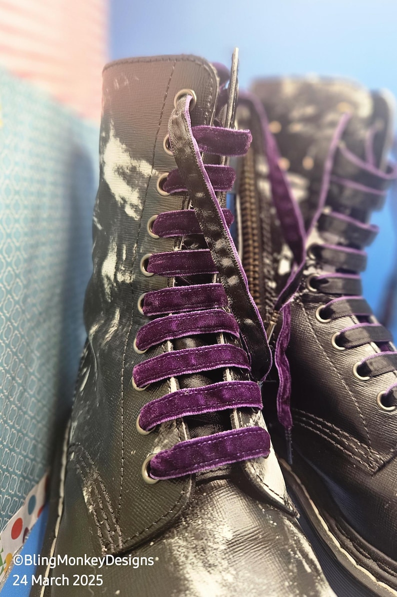 May include: A pair of black leather boots with purple velvet laces. The boots have a white and black tie-dye pattern on the upper part of the boot.