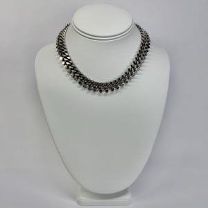 May include: A silver-toned curb chain necklace featuring a series of small, dangling circular charms attached along the bottom edge of the links. The necklace has a polished metallic finish and is displayed on a white neck-shaped jewelry stand.