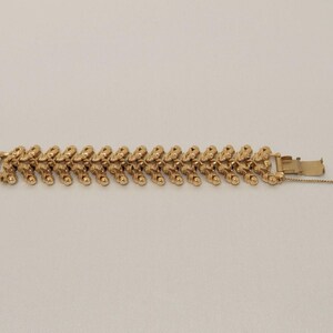 May include: A gold bracelet featuring a repeating pattern of textured links. The bracelet has a secure clasp with a safety chain. The design is symmetrical and the bracelet is displayed on a neutral background.