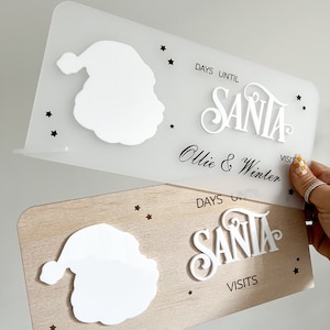 May include: White wooden countdown sign with a Santa silhouette and the text "Days Until Santa Ollie & Winter Visit".