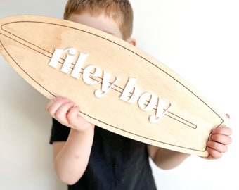 May include: A wooden surfboard with the text "riley boy" in white letters. The surfboard is being held by a child.