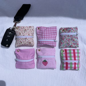 Puede incluir: Seis pequeñas bolsas con cremallera de varios patrones en rosa y blanco. Las bolsas están hechas de tela y tienen un cierre de cremallera. Los patrones incluyen cuadros, flores y rayas.