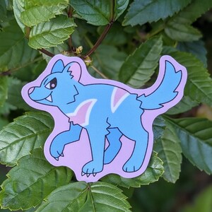 May include: A blue and pink cartoon sticker of a wolf-like creature with a pink background. The creature has a white stripe on its chest and a pink stripe on its back.