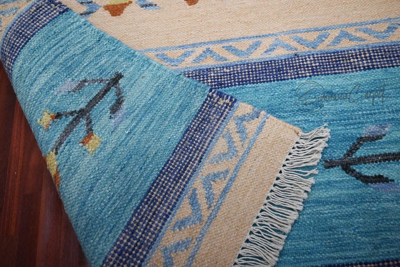Handwoven kilim rug in blue and beige with tribal geometric patterns; flatweave wool, fringed edge, boho ethnic decor.